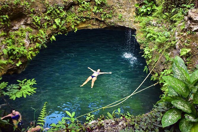 A swimmer floating in an open Yucatan cenote ringed by jungle